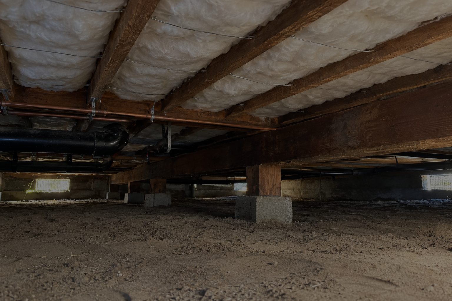 Under a raised house after the job: white insulation held up between the floor joists, the dirt floor raked clean