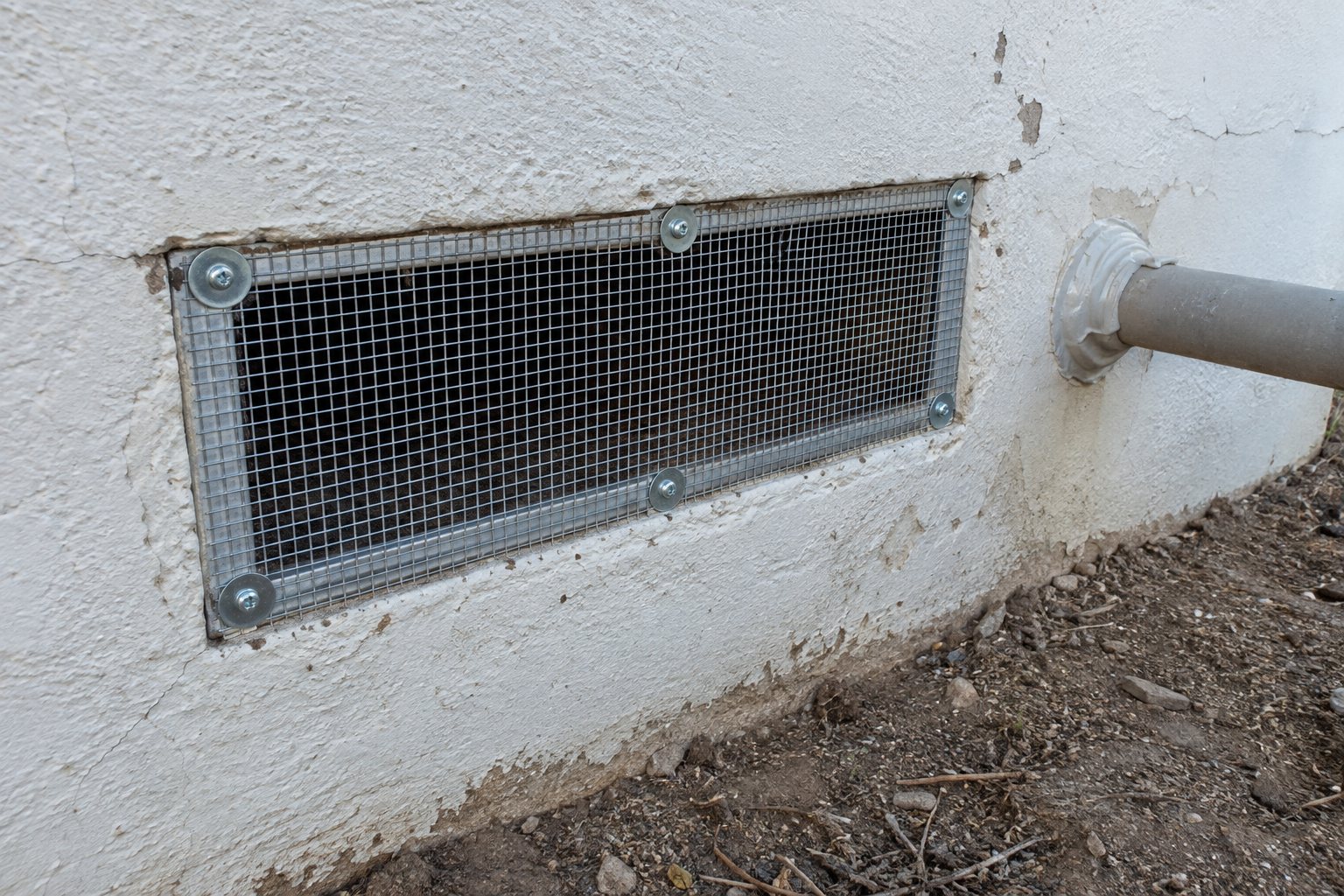 A vent on a stucco wall fitted with new steel mesh